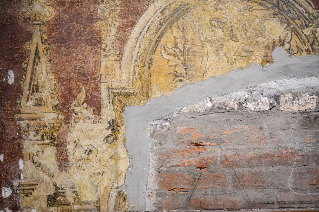 A partially cleaned fresco wall showing the sharp boundary between the untreated surface and the section already restored