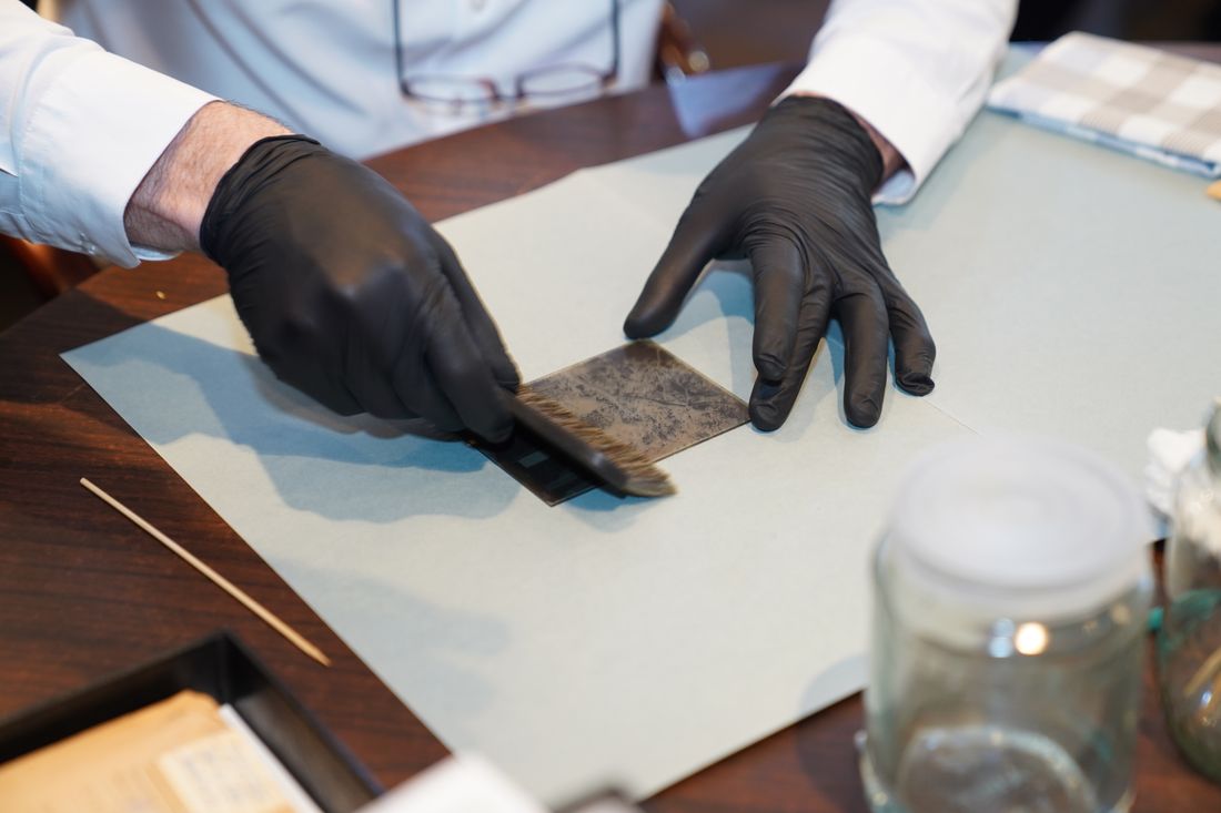 Gloved hands using a fine tool to work on a small area of a print during a conservation treatment