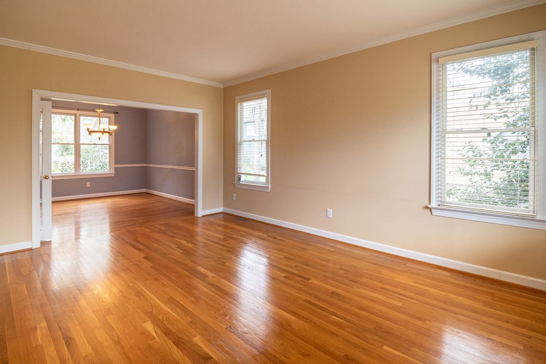 An empty room with hardwood floors, tall windows, and plain walls