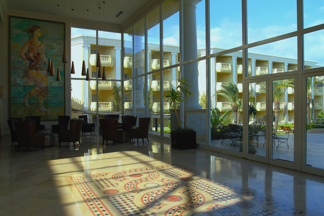 Large artwork and patterned floor mosaic in a bright contemporary lobby with seating and glass walls.