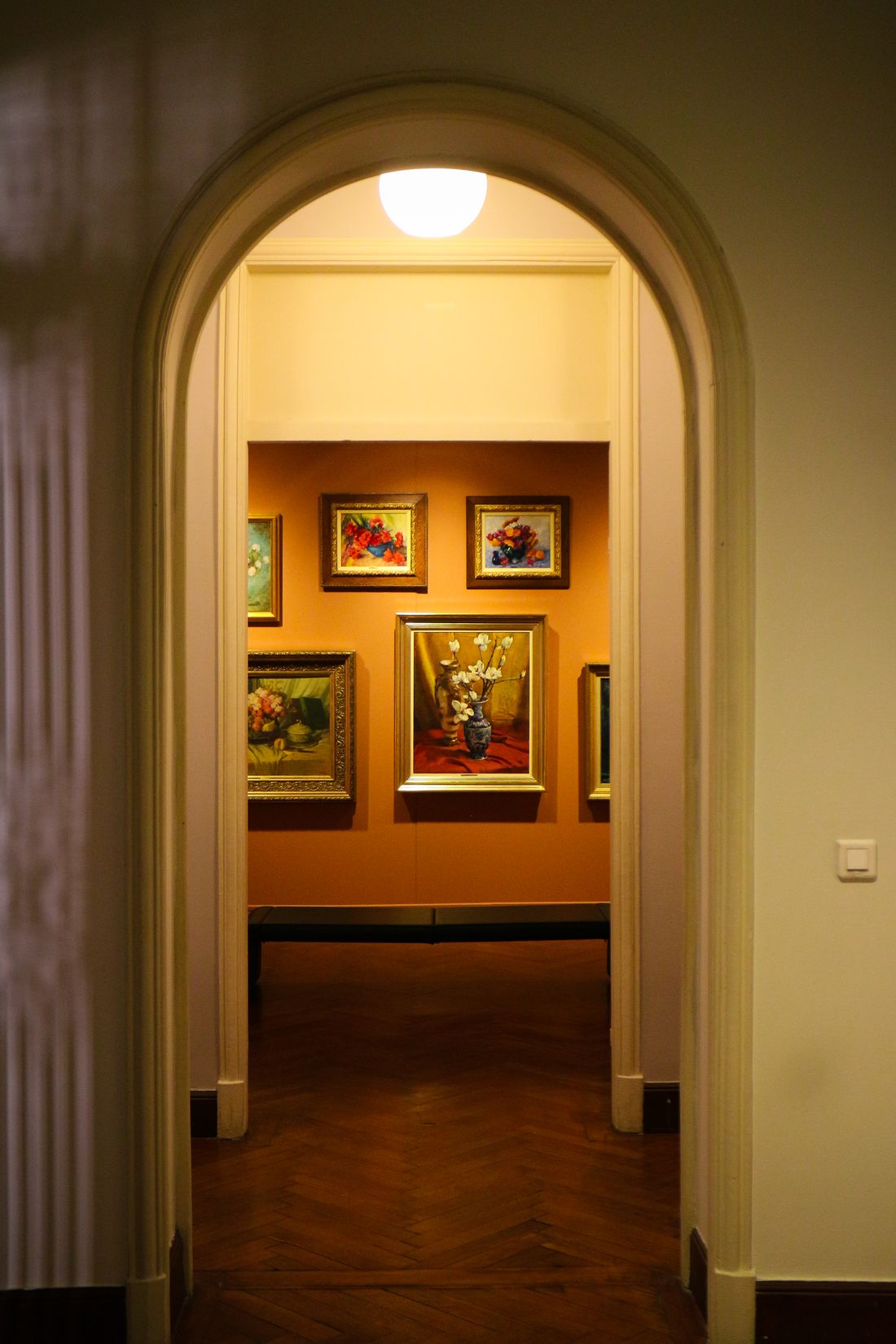 A quiet art-gallery corridor with framed paintings lining both walls.