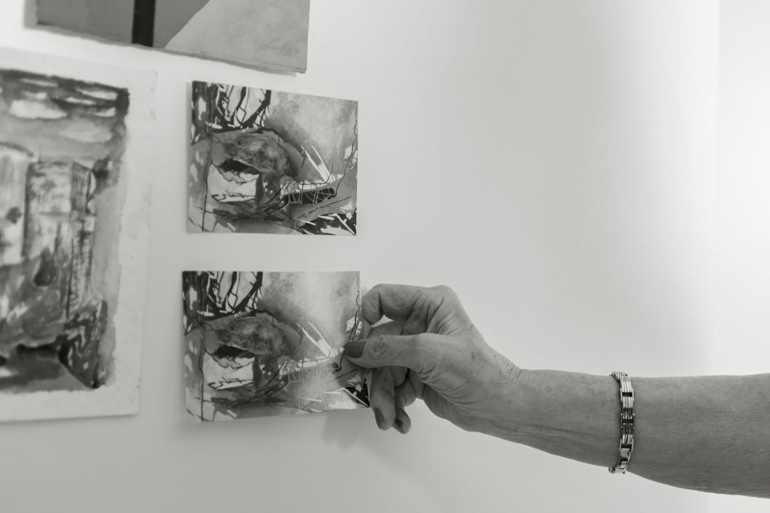 A hand placing a small monochrome art print on a gallery wall next to another framed piece