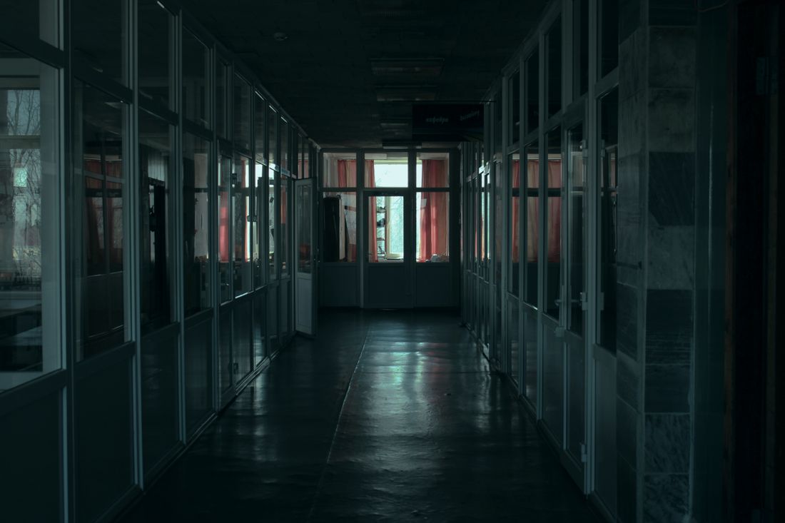 Gloomy indoor corridor with glass partitions and dim lighting in a modern office building.