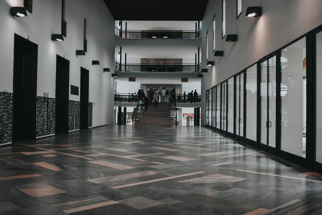 A grand, multi-story institutional lobby with marble floors and a small crowd of visitors gathered near a wide staircase at the far end