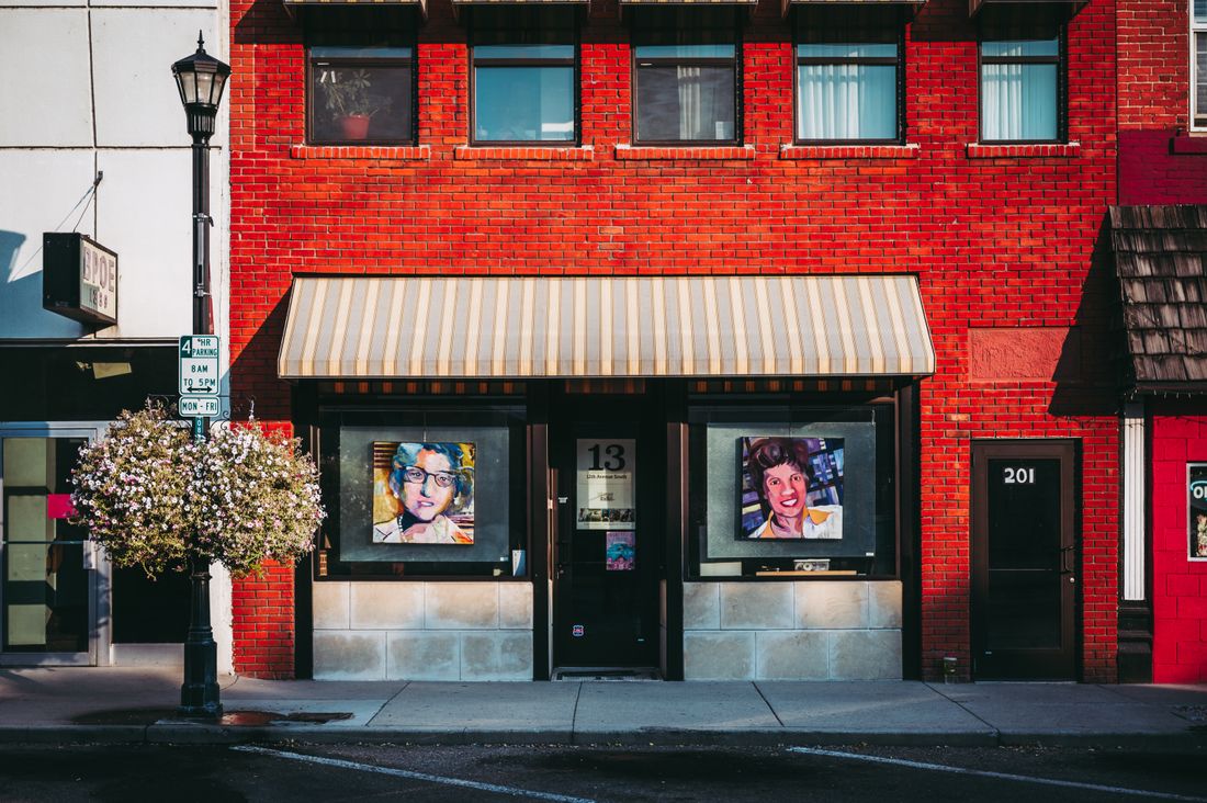 A red brick storefront building with framed artwork visible in the ground-floor windows