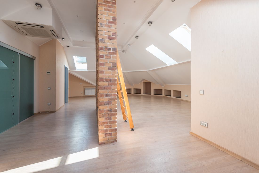 An empty loft room with skylights, a bare brick pillar and a wooden ladder