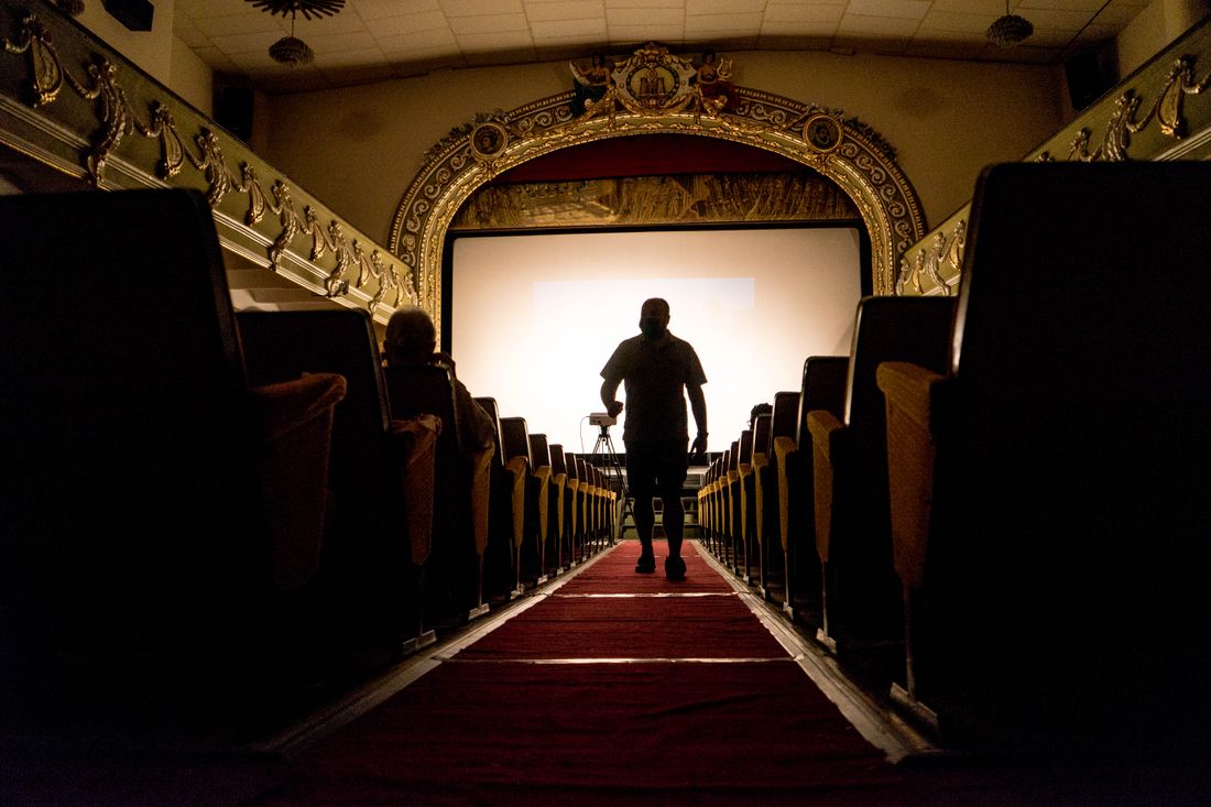 A silhouetted figure walking down a center aisle between rows of seating toward a lit screen