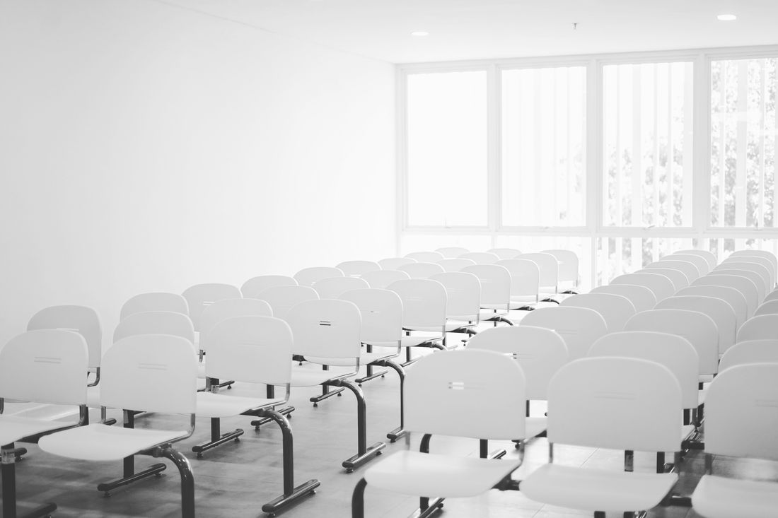 Rows of empty white chairs arranged in a bright room before a talk.