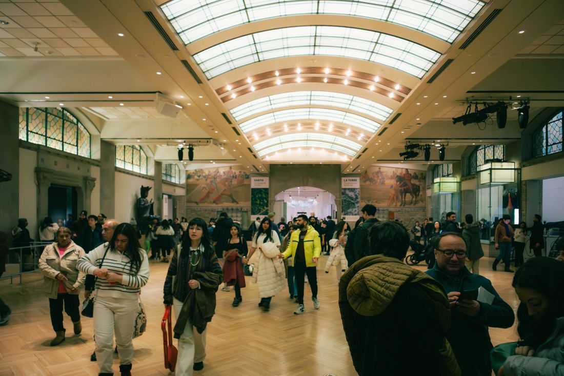 Crowd of visitors walking through a wide exhibition hall lined with framed artwork under an arched glass ceiling