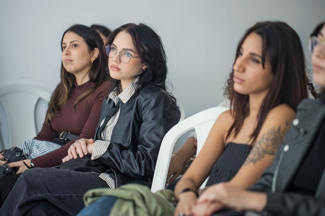 A row of seated visitors listening attentively during an indoor talk, their focused expressions representing the audience during a discussion or crit segment.