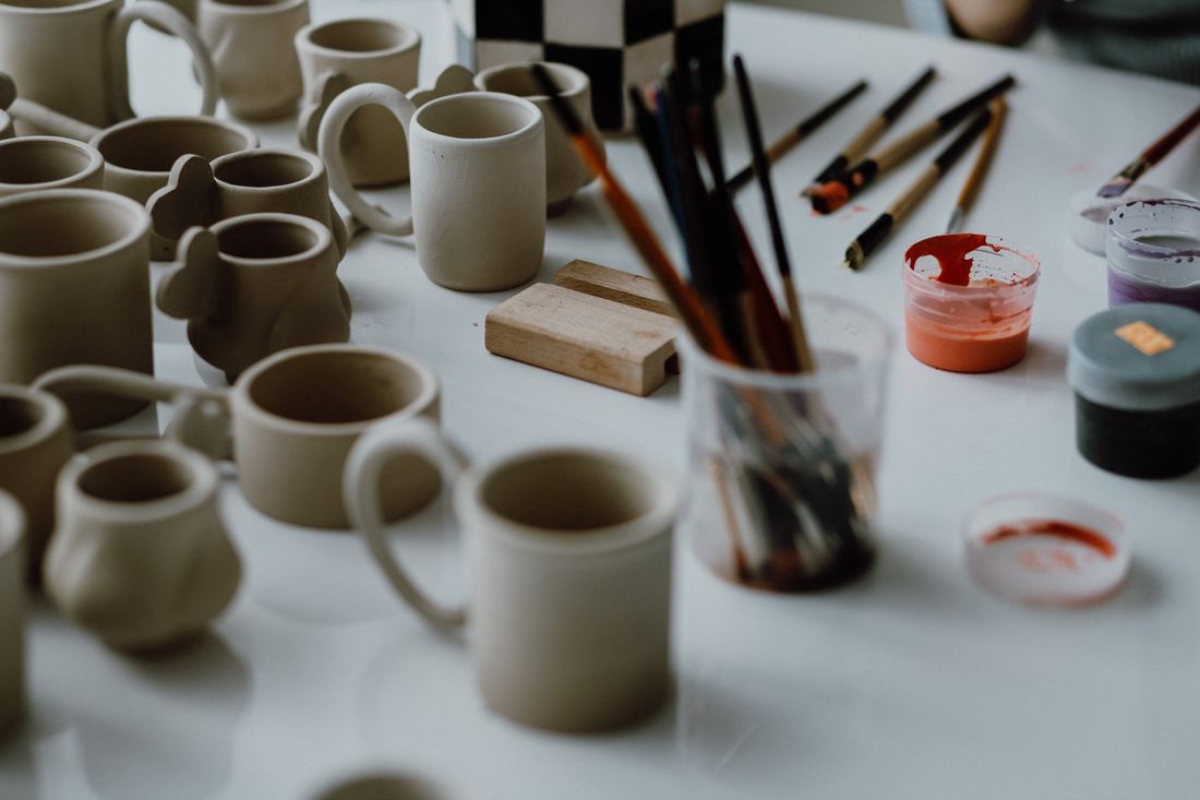 Unglazed ceramic mugs and pottery tools arranged on a studio table, representing work still in progress rather than a finished piece.