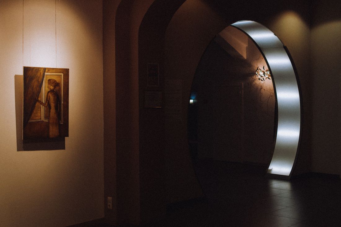 A single painting lit and hanging on a gallery wall beside an empty archway, no visitors in the room