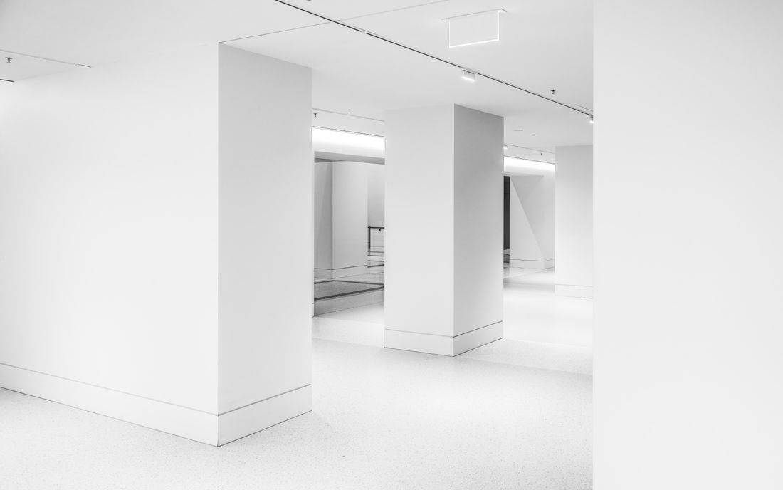 An empty minimalist white gallery interior with bare walls and columns, no artwork on display