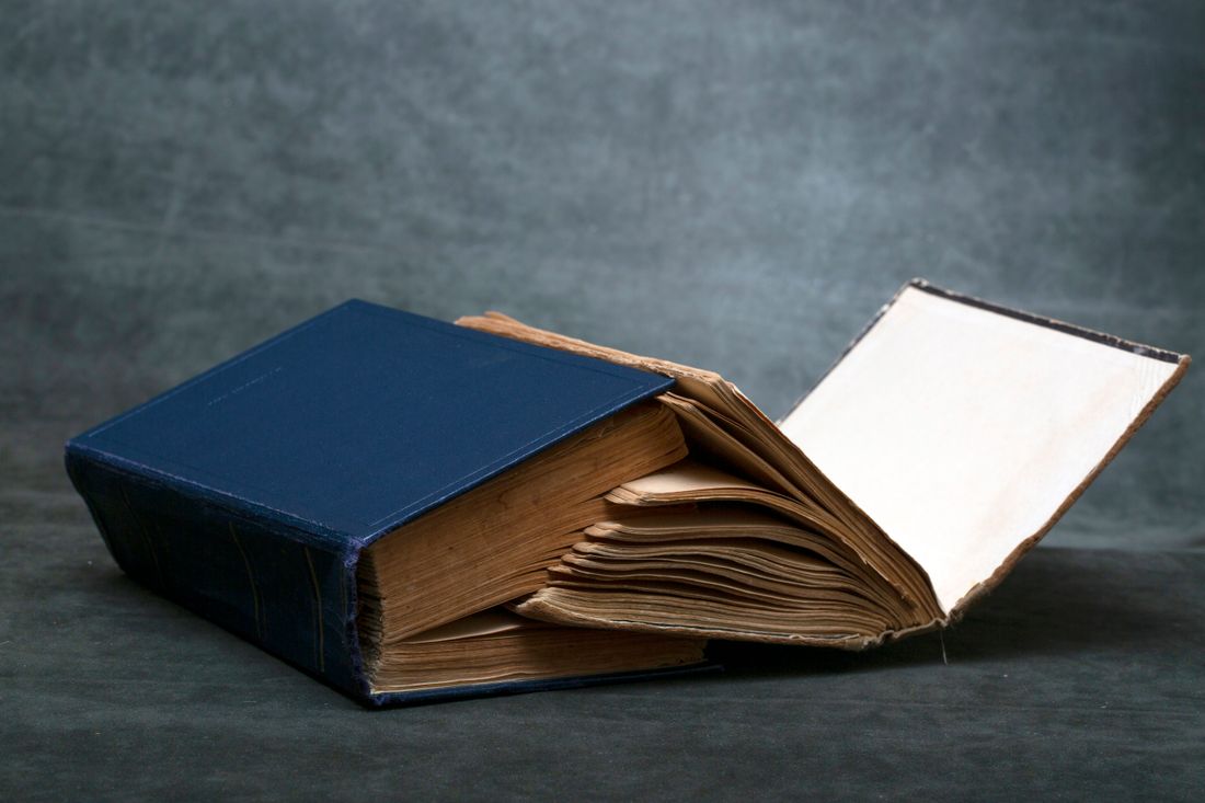 A worn hardcover book resting open with its pages fanned unevenly away from a visibly stressed spine