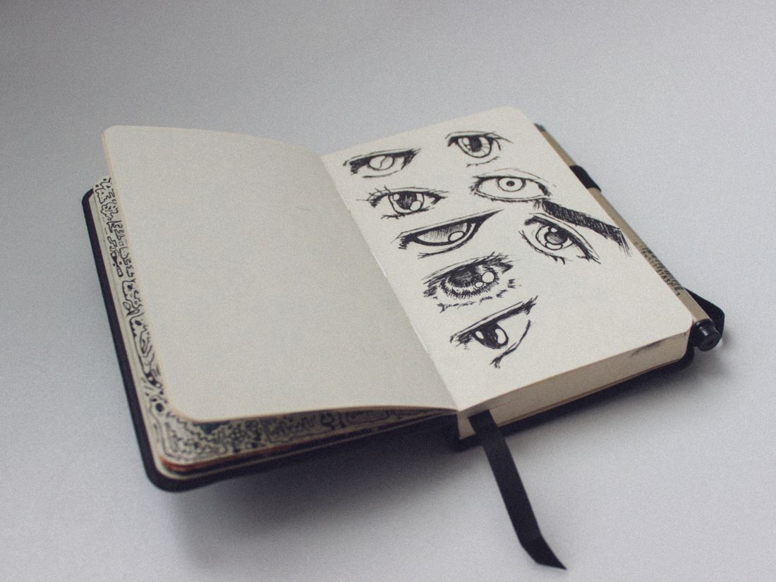 An open sketchbook lying on a surface, showing a page of detailed pencil sketches with the spine and decorated page edges visible