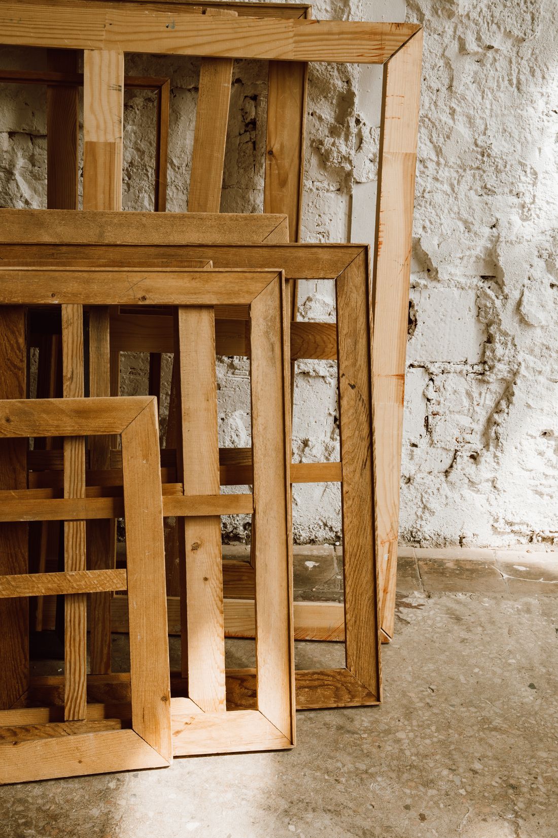A small collection of empty wooden picture frames of different sizes leaning together against a textured wall