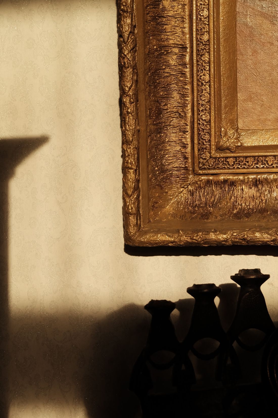 A tight detail on the corner of an ornate gold picture frame's molding, hung on a wall in warm light