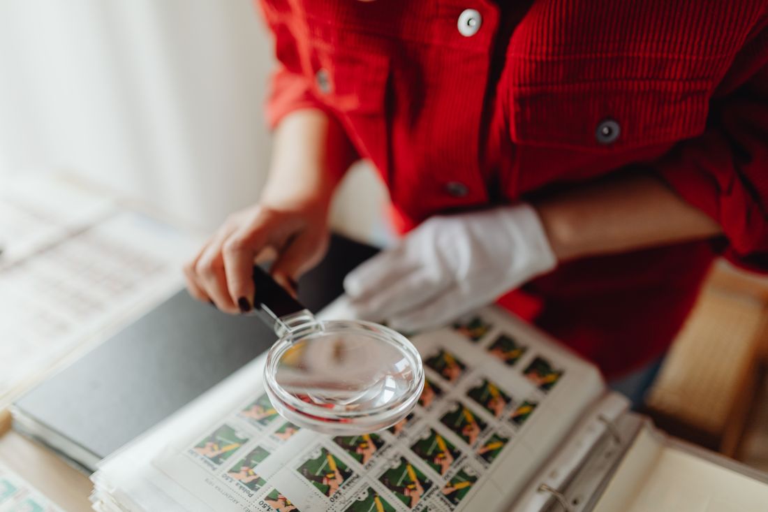 A person closely examines postage stamps with a magnifying glass, revealing intricate details.