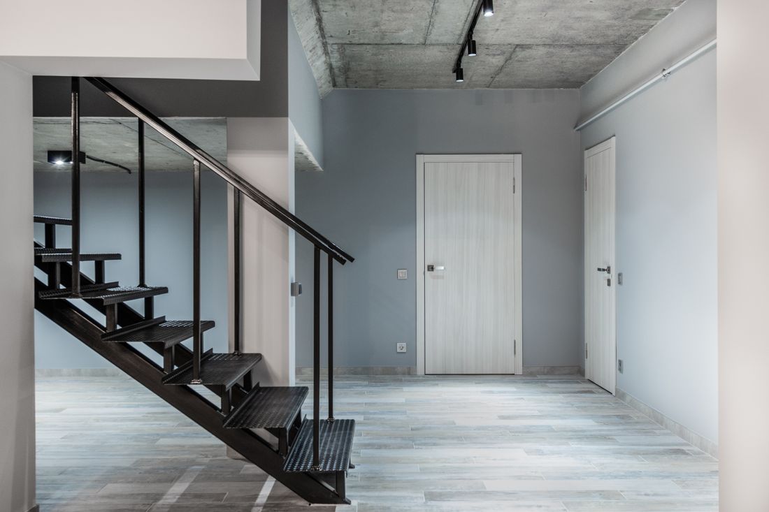 A narrow interior staircase photographed from the bottom, leading up toward closed doors, plain walls, no furniture in the path