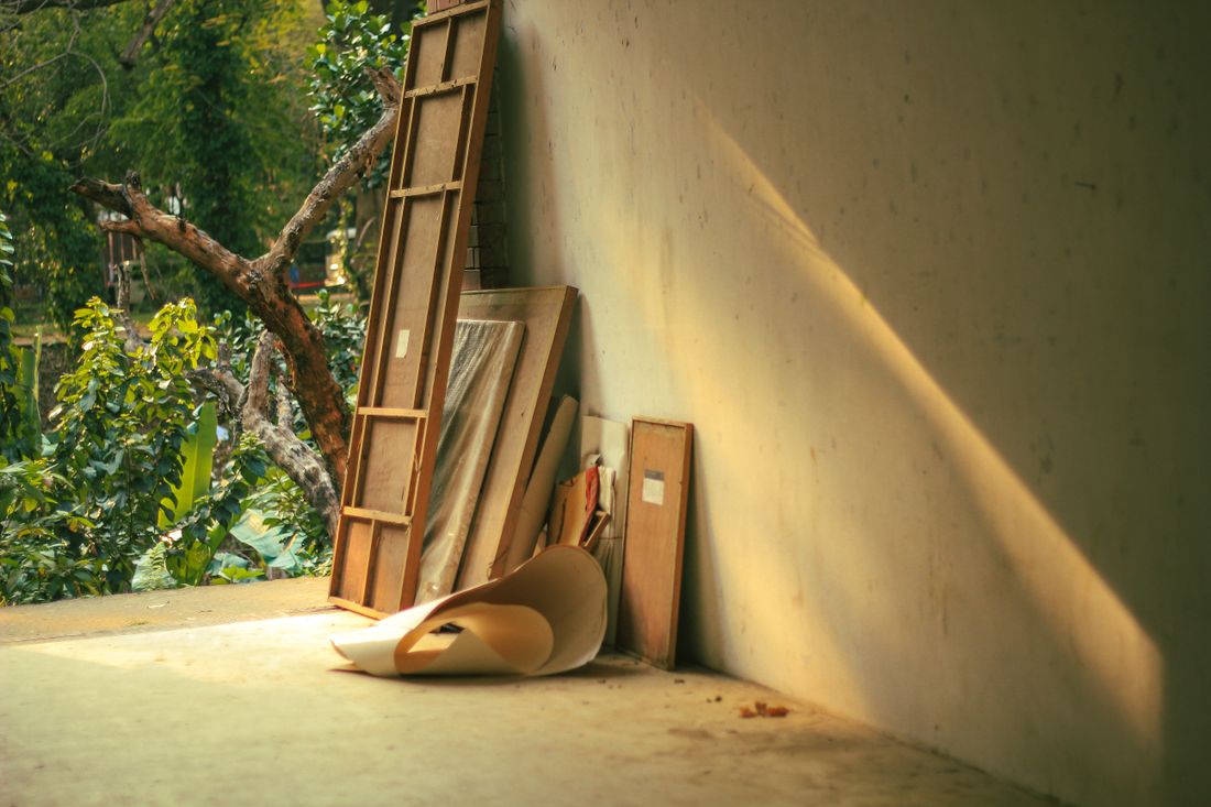 Wooden frames and a rolled canvas leaning against a wall in a sunlit corner, quiet and unstaged