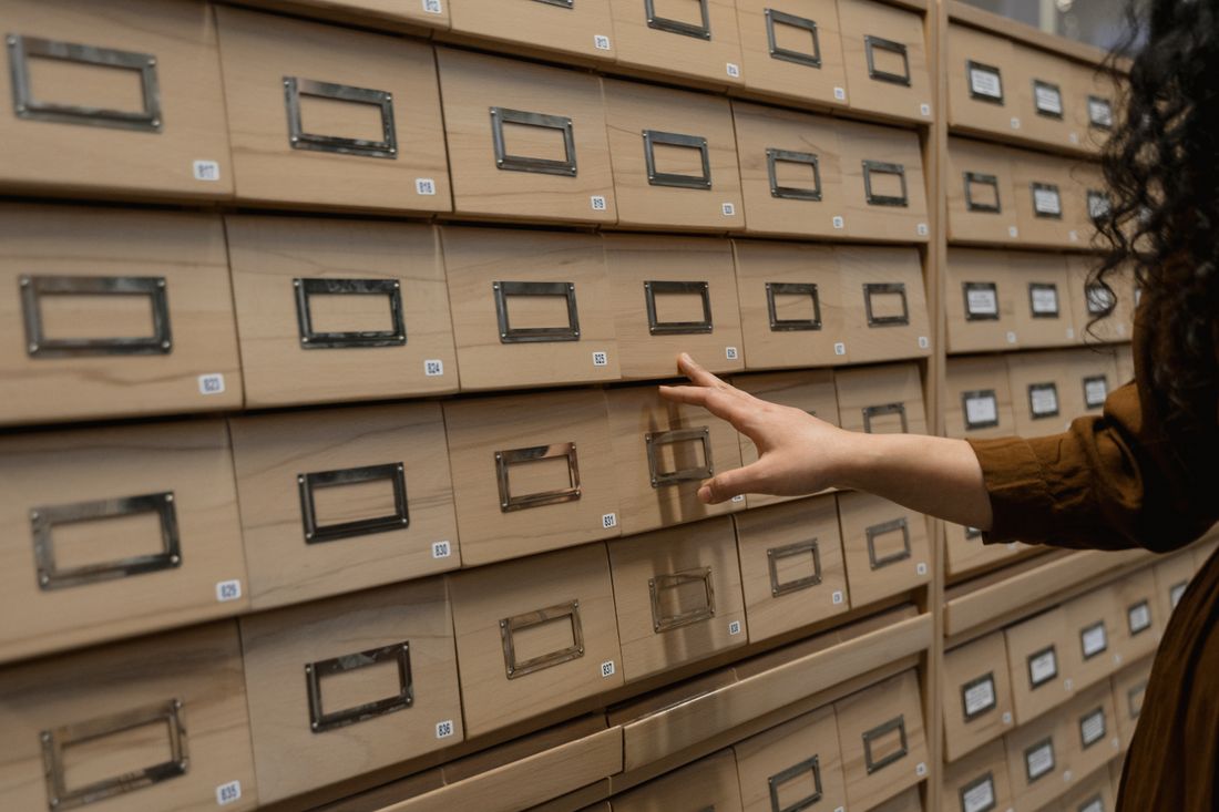 A hand reaching toward a wall of small wooden archive drawers, face out of frame