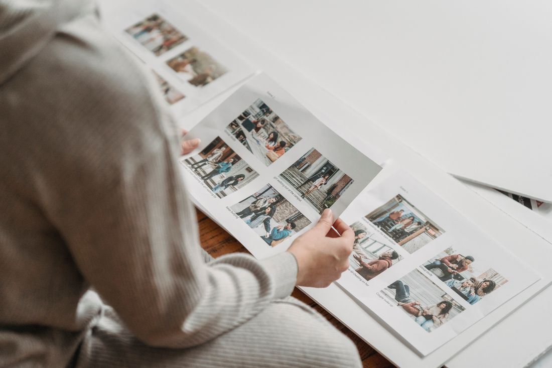 A person from behind reviewing printed photo contact sheets spread across a desk