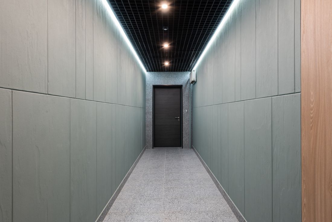 A narrow plain-walled corridor with a hard terrazzo floor leading to a single closed door