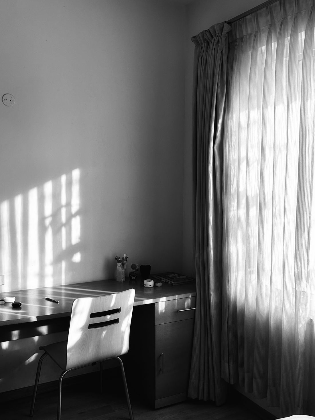 An empty desk and chair in a plain, quiet office corner lit by soft window light, no one present