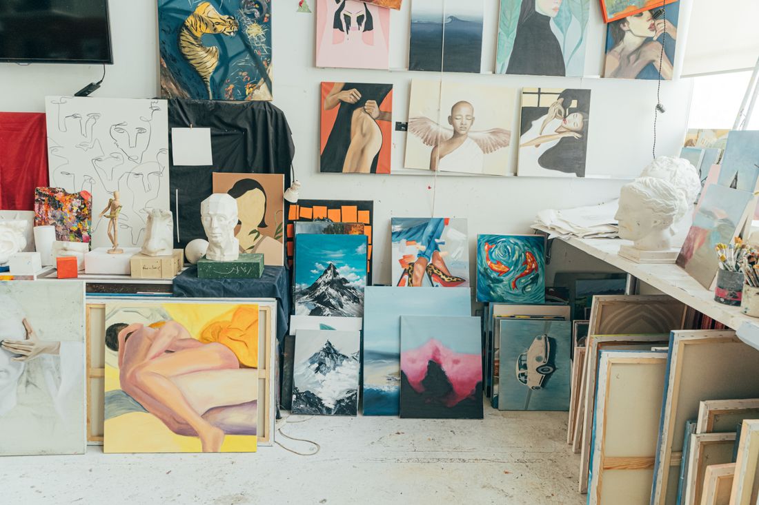 A working art studio wall densely covered with finished paintings, sculptures, and works in progress