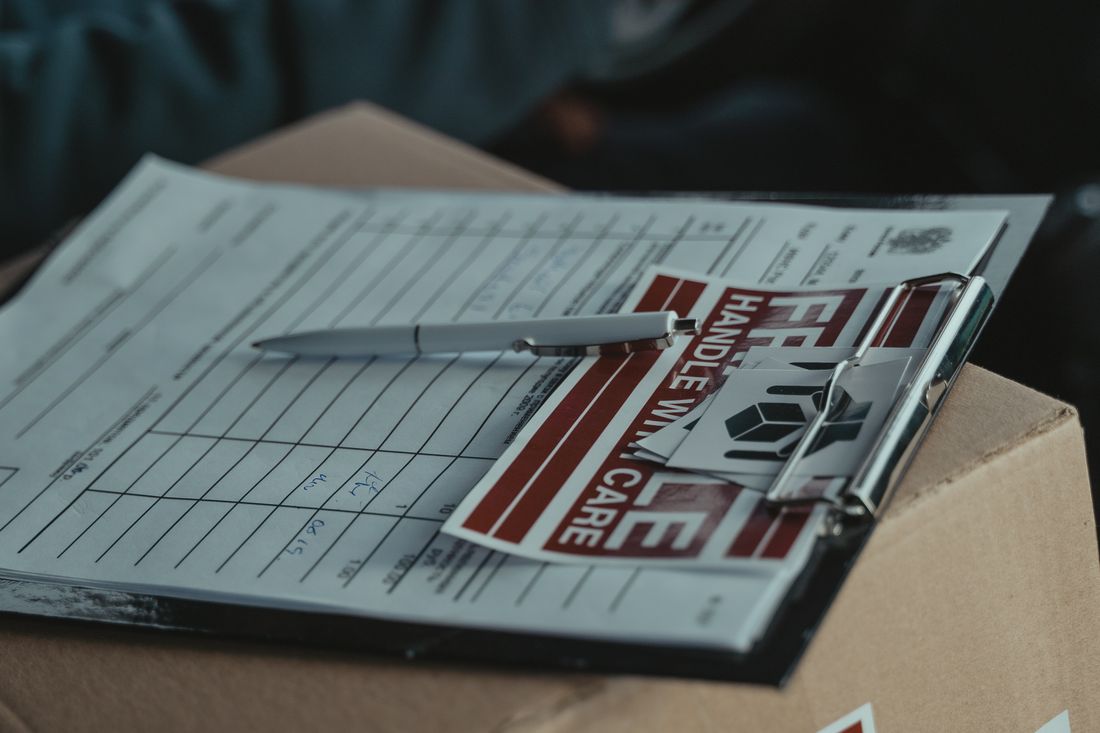 A clipboard with a shipping form and a handle-with-care sticker resting on a cardboard box