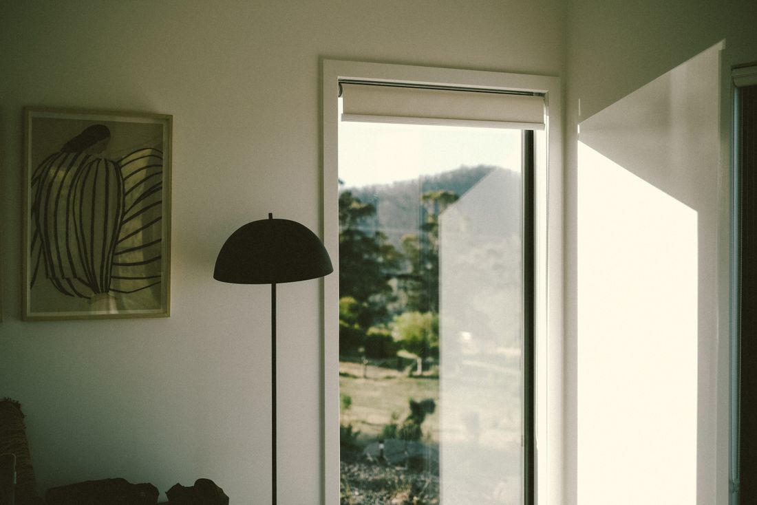 A framed artwork on a wall next to a floor lamp, with bright window light spilling in from the side