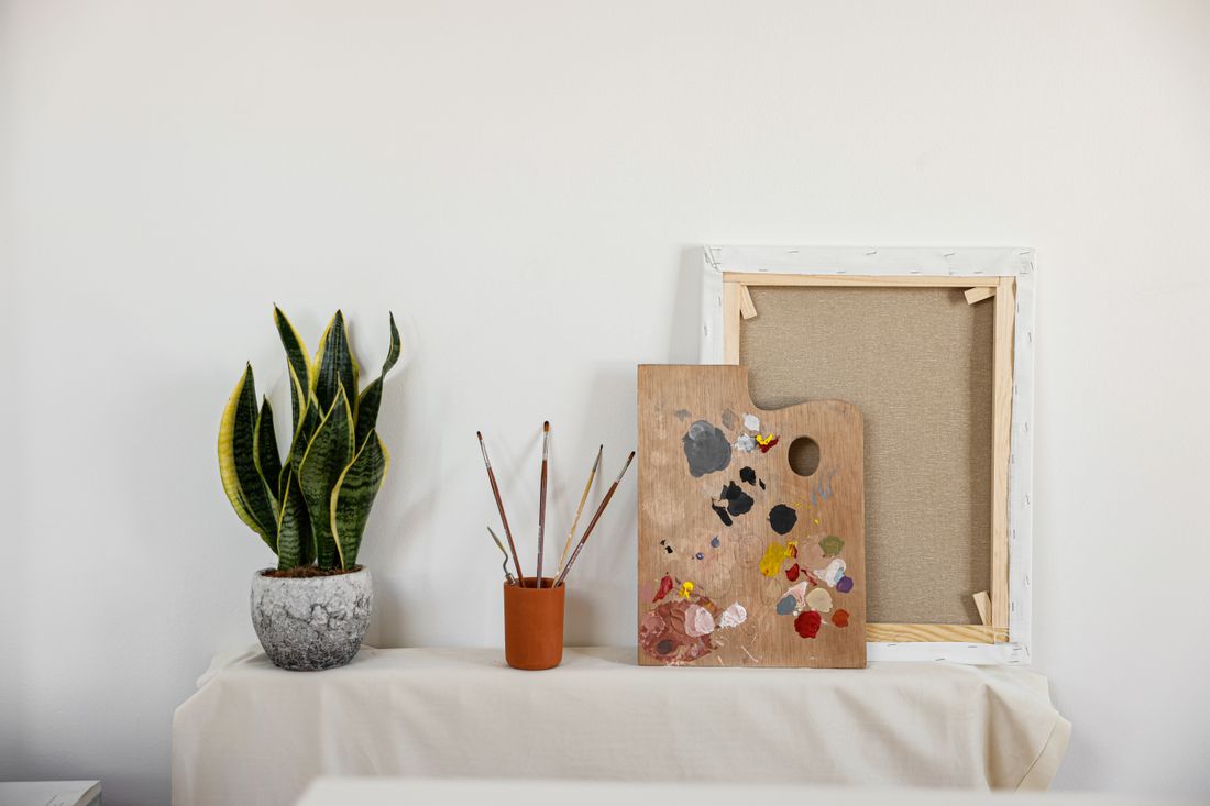 A minimalist studio corner with an empty canvas, paintbrushes, and a small potted plant