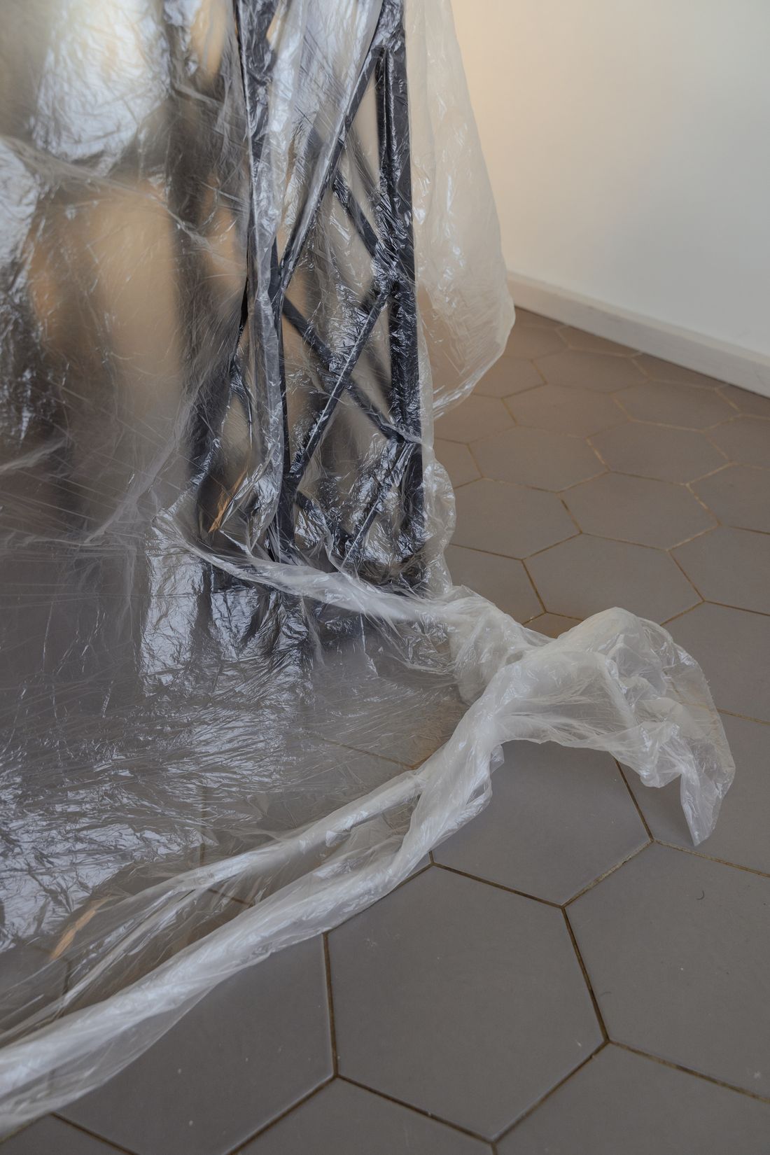 Furniture wrapped tightly in clear plastic sheeting on a tiled floor, protective packing material bunched at the base
