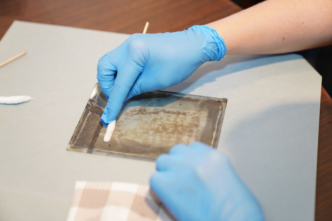 Gloved hands carefully examining and handling artwork at close range on a work surface