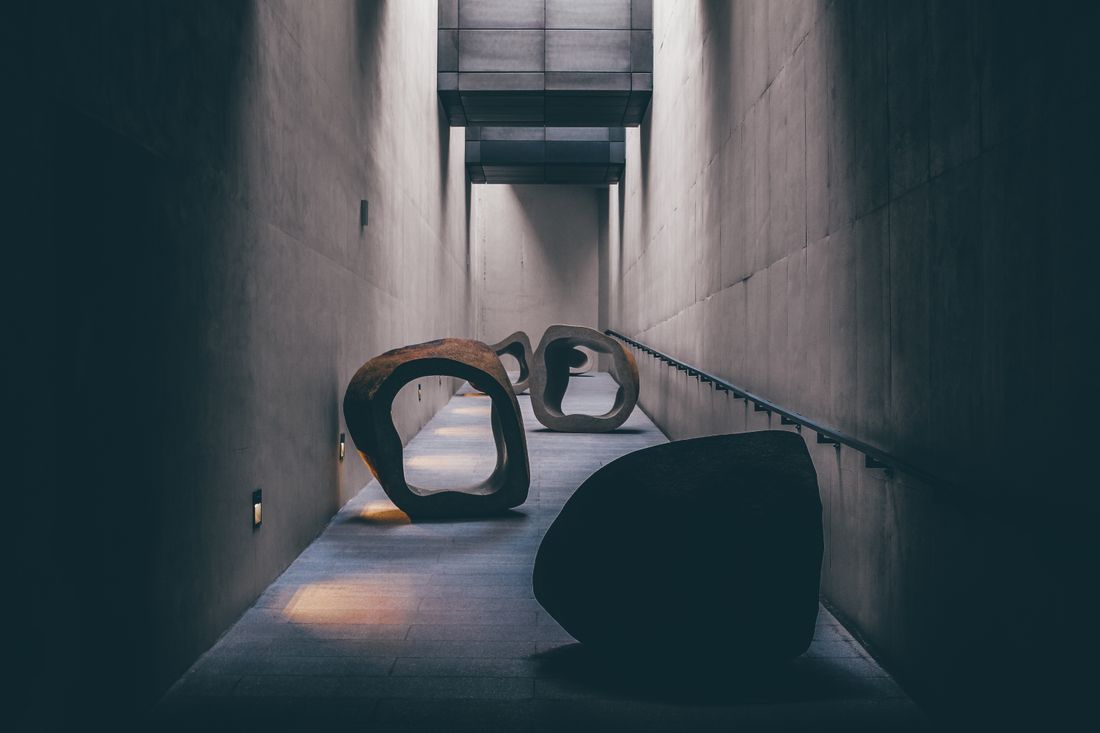 Large curved sculptural forms fill a narrow concrete corridor, giving a quiet, unpeopled sense of scale.
