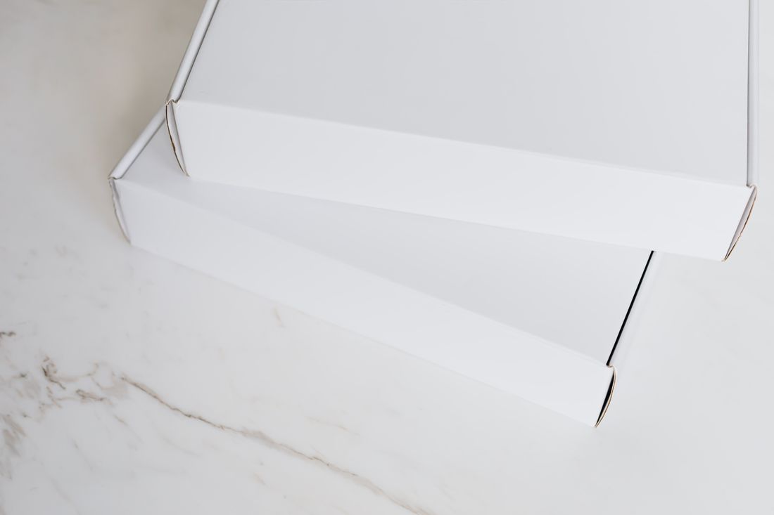 Two flat closed white boxes stacked at an angle on a plain marble tabletop