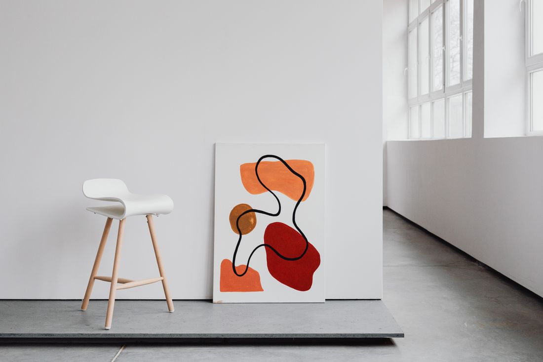 An abstract painting leaned against a plain white wall in a bright, uncluttered room