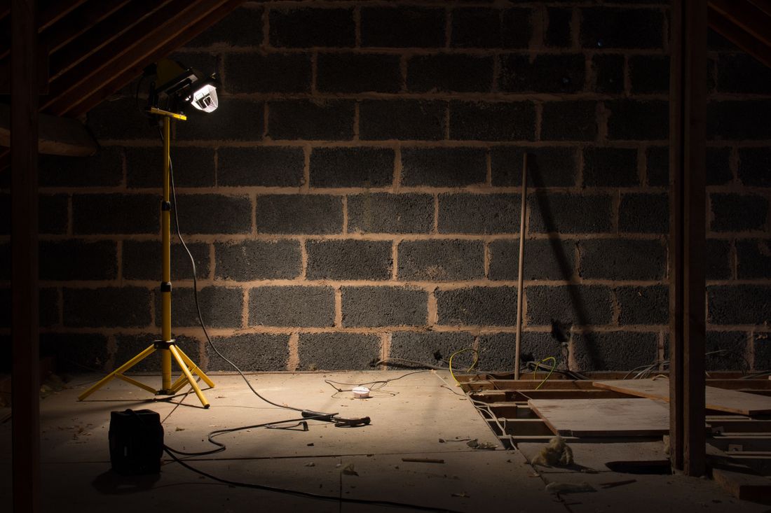 A single portable work light on a stand illuminating a dim, unfinished room with a concrete floor and cinderblock walls.