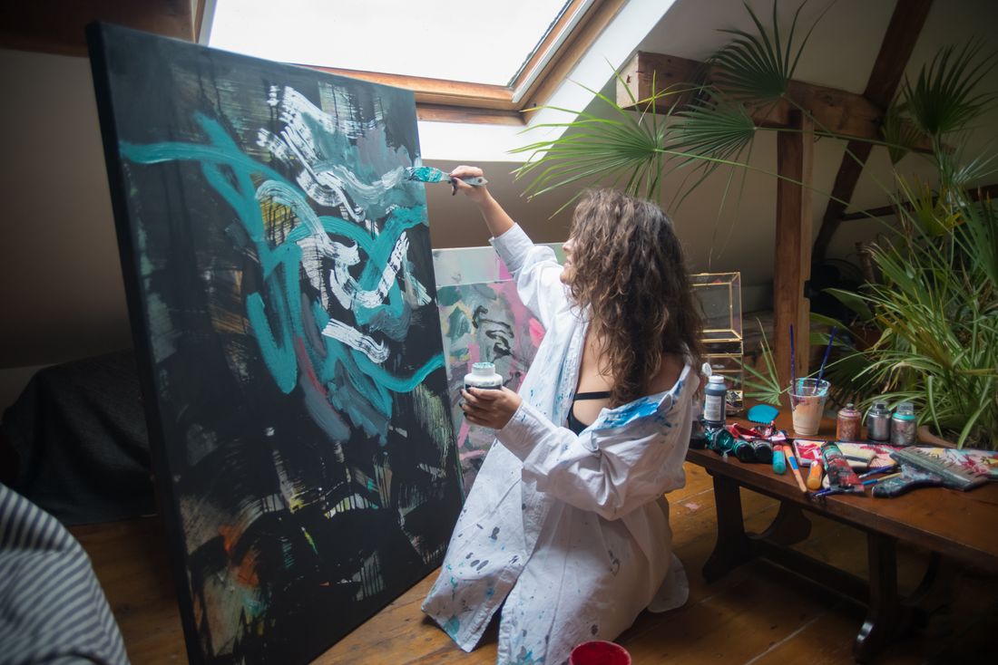 An artist working on a large canvas propped against a wall in a sunlit studio