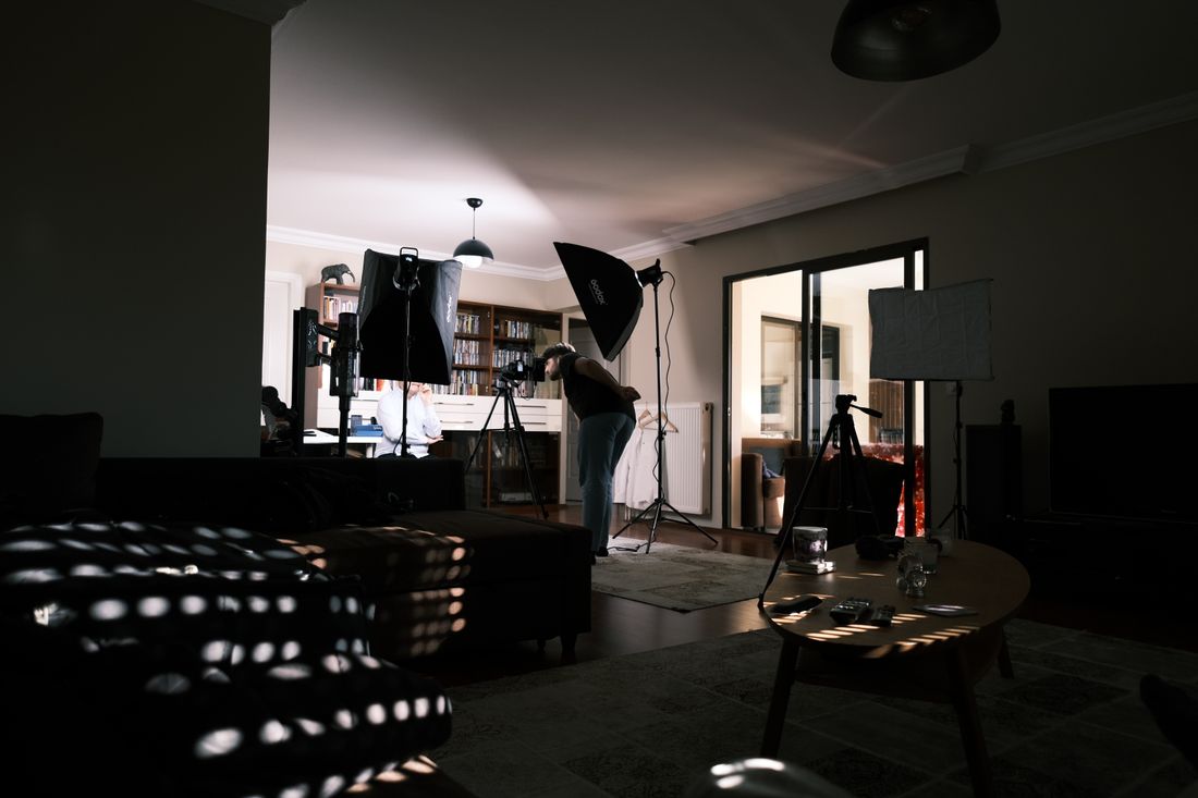 A person adjusting camera and softbox lighting equipment spread across a spacious room
