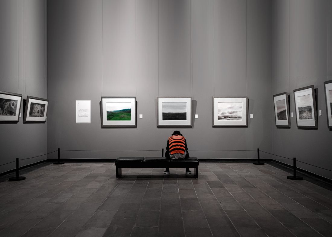 A visitor sits on a bench viewing a row of framed photographs displayed on a gallery wall
