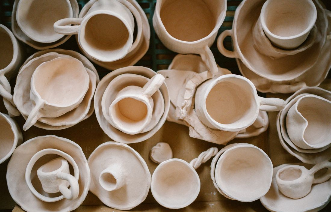 Overhead view of many unfinished, unfired clay cups and bowls crowded together on a board