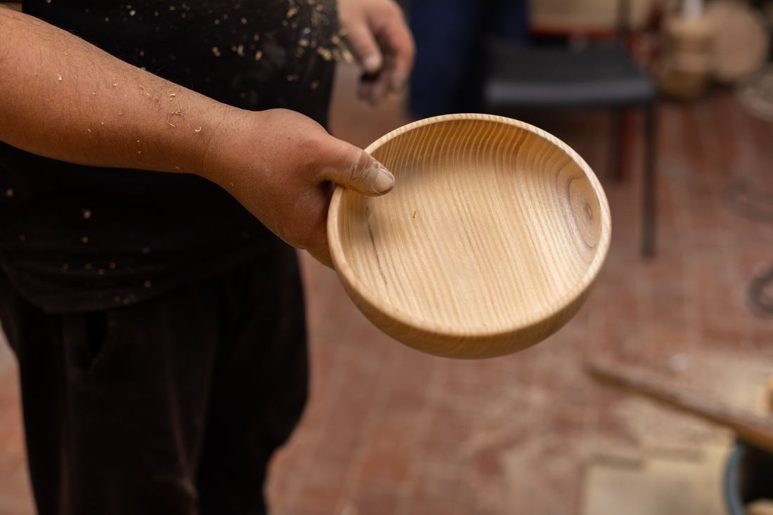 A hand holding a finished handmade wooden bowl, representing a workshop participant's finished result.