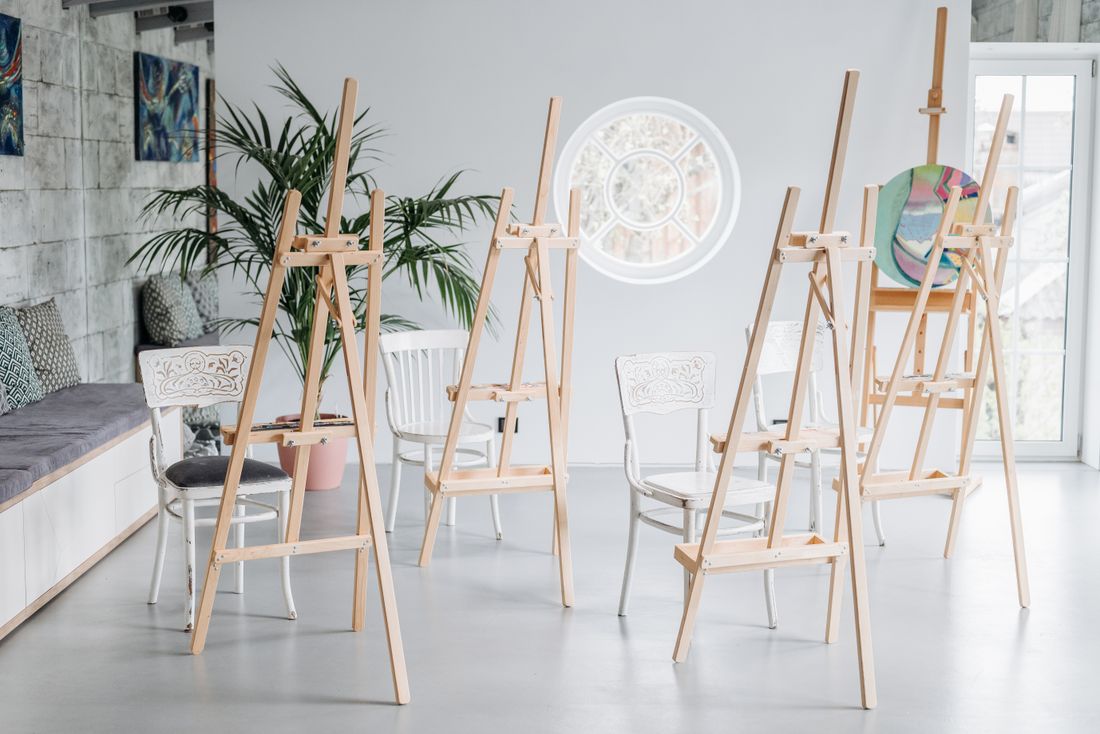 A sunlit workshop room with wooden easels and white chairs set up for a class, showing the space before students arrive.