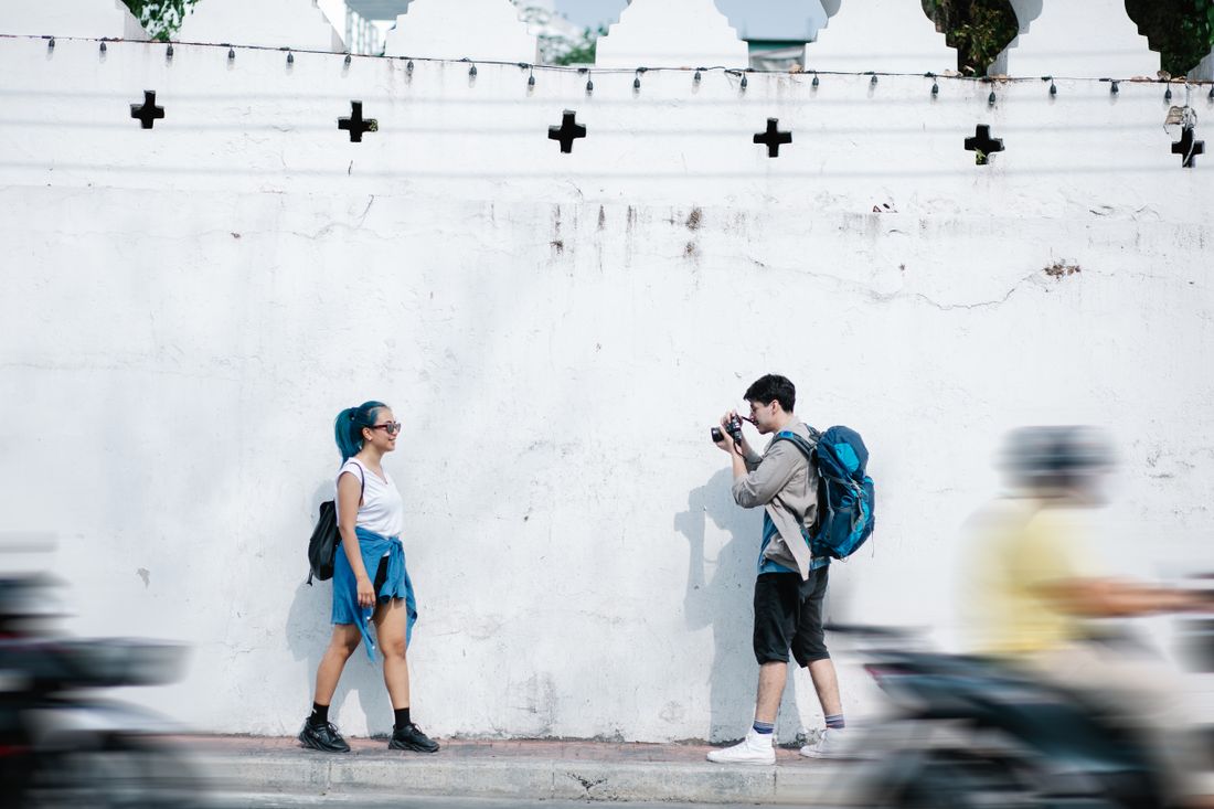 A photographer photographing a subject on a city sidewalk as traffic passes