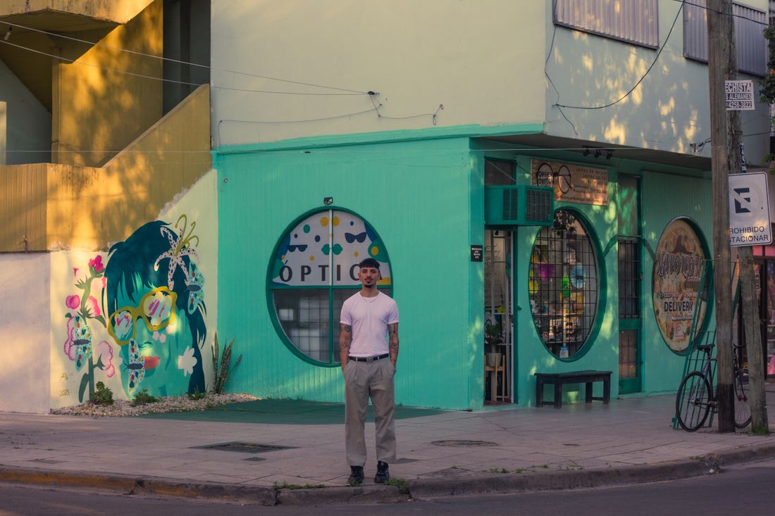 A man standing on a sunlit street beside a colorful mural