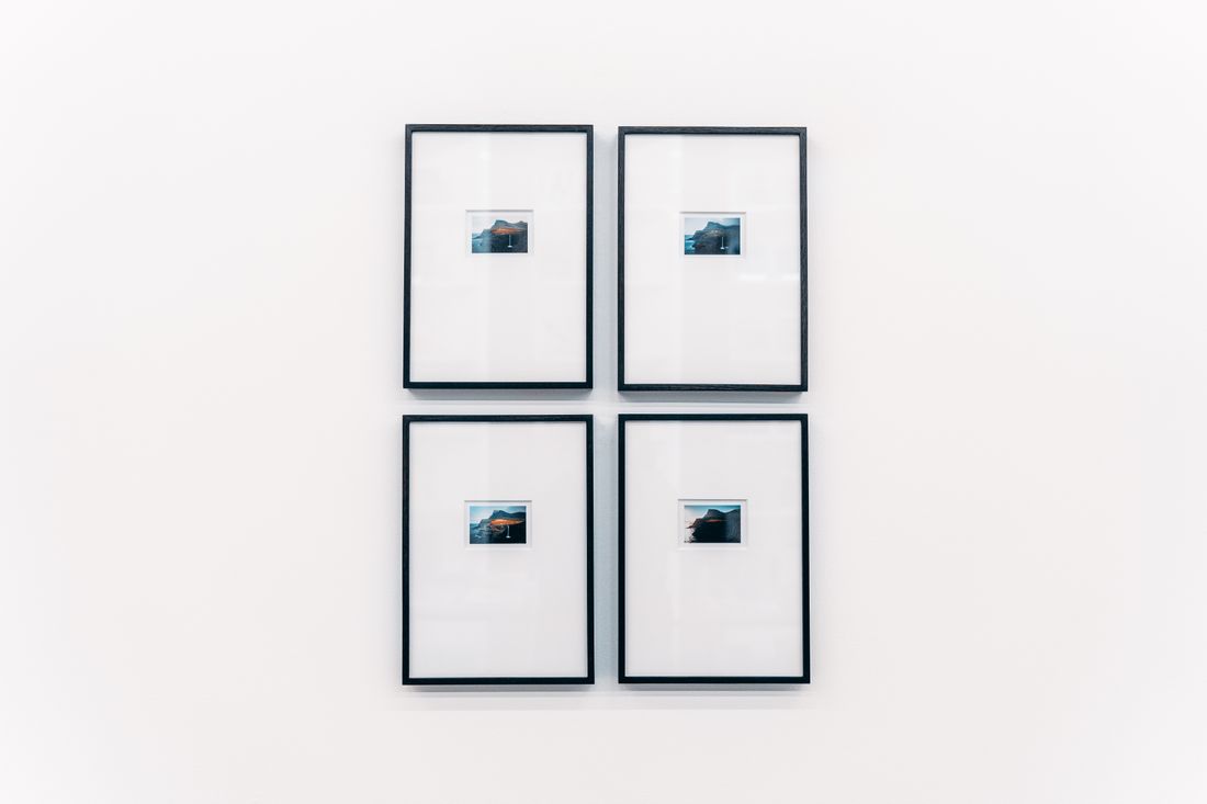 Four small framed photographs evenly spaced on a plain white gallery wall, softly lit and free of people.
