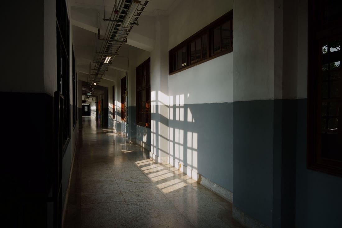 A quiet, empty corridor in a modern building, window light casting long geometric shadows across the wall and floor.