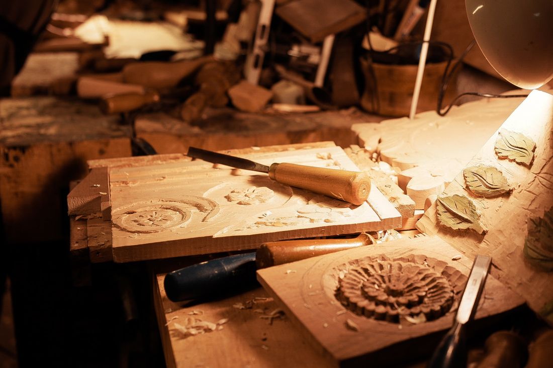 Warm side-lit view of hand-carved wooden panels with tools resting on a workbench