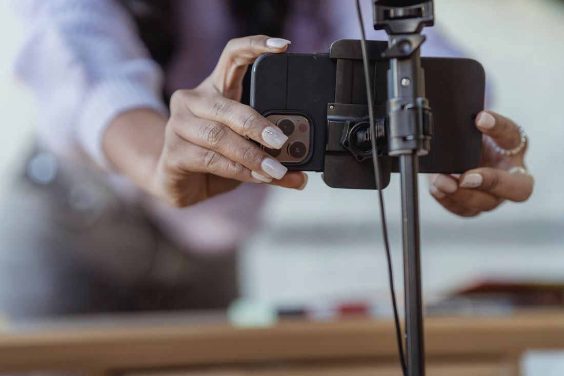Hands mounting a smartphone onto a tripod clamp in a soft-focus workspace